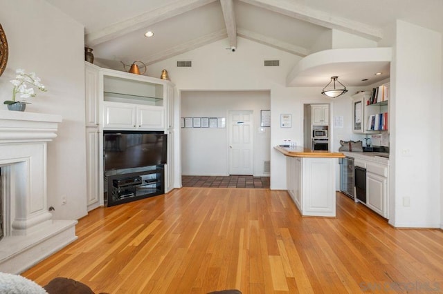 kitchen with pendant lighting, butcher block countertops, white cabinetry, vaulted ceiling with beams, and light wood-type flooring