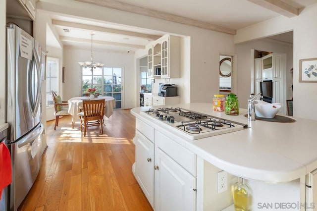 kitchen featuring beamed ceiling, stainless steel appliances, decorative light fixtures, and white cabinets