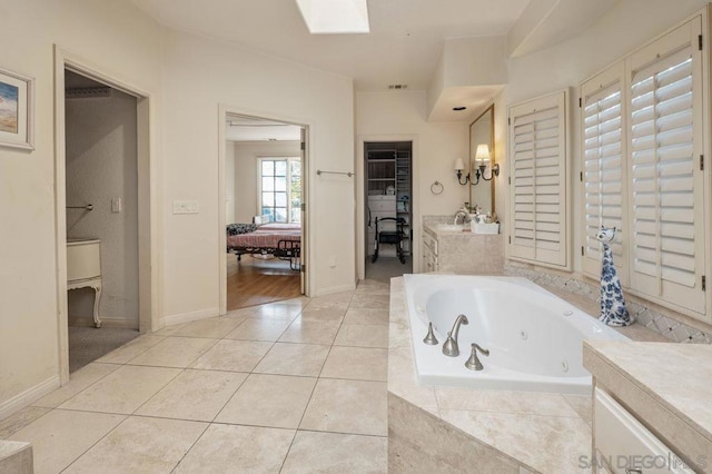 bathroom with vanity, tiled tub, a skylight, and tile patterned floors