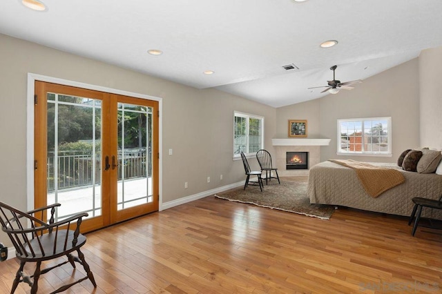 bedroom featuring a tile fireplace, lofted ceiling, access to exterior, light hardwood / wood-style floors, and french doors