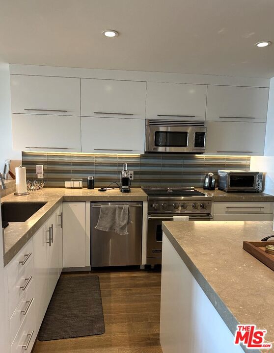 kitchen featuring sink, white cabinetry, dark hardwood / wood-style floors, stainless steel appliances, and backsplash