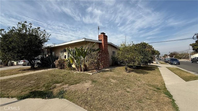 view of side of home featuring stucco siding, a lawn, and a chimney