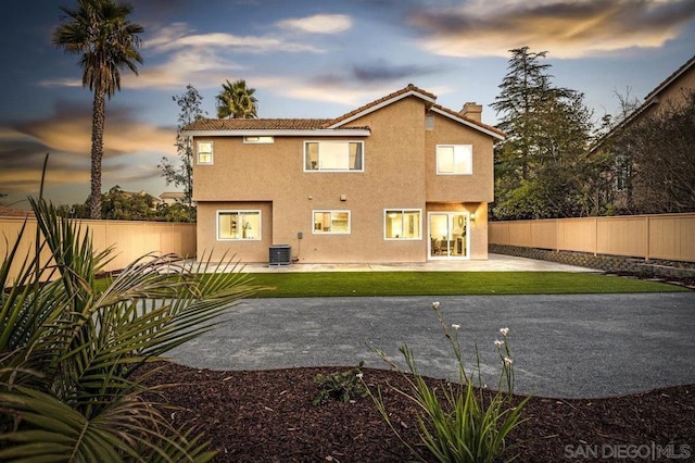 back house at dusk featuring a patio, central AC, and a lawn