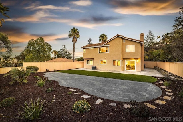 back house at dusk with a patio, central AC unit, and a lawn