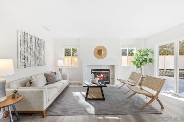 living room with a tiled fireplace, a healthy amount of sunlight, and light hardwood / wood-style flooring