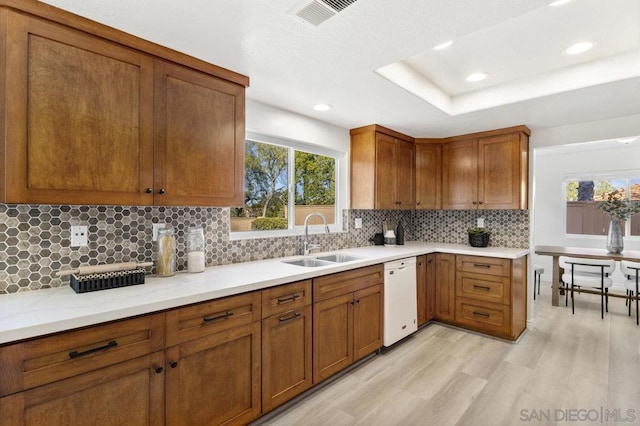 kitchen featuring sink, backsplash, white dishwasher, a raised ceiling, and light wood-type flooring