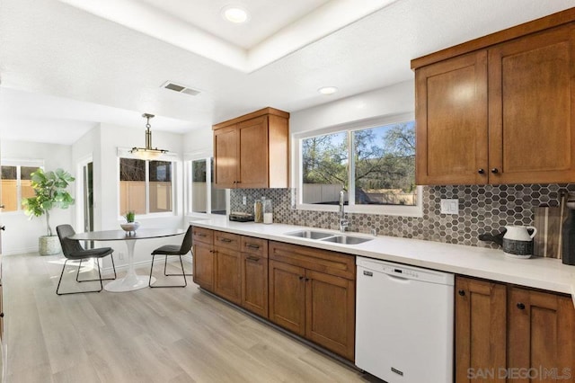 kitchen featuring sink, tasteful backsplash, hanging light fixtures, light hardwood / wood-style flooring, and white dishwasher