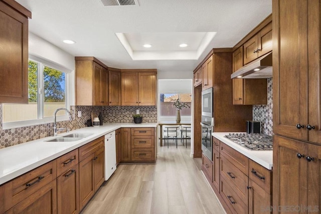 kitchen with sink, light hardwood / wood-style flooring, dishwasher, stainless steel gas cooktop, and a raised ceiling