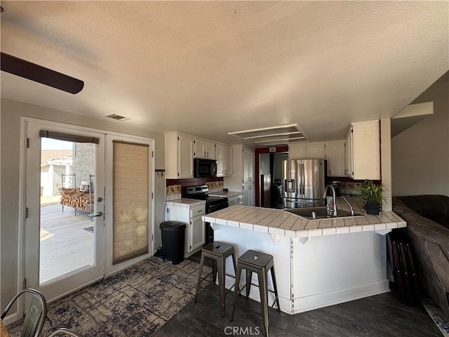 kitchen with sink, a breakfast bar area, white cabinetry, stainless steel appliances, and tile countertops