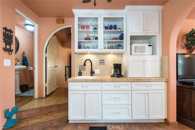 bar featuring dark wood-type flooring, sink, white cabinets, light stone countertops, and backsplash