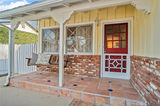 view of exterior entry with brick siding, board and batten siding, and fence