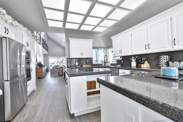 kitchen with stainless steel appliances, tasteful backsplash, white cabinets, a kitchen island, and dark stone counters