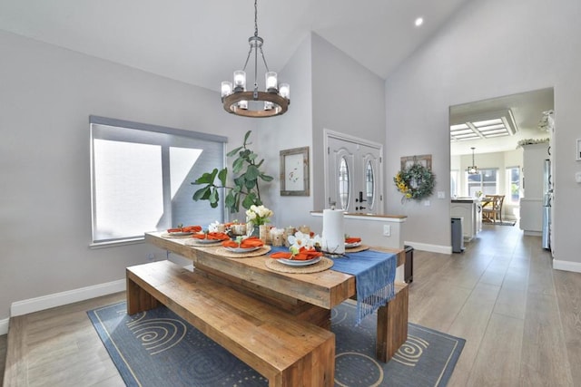 dining area with high vaulted ceiling, light wood-type flooring, and an inviting chandelier