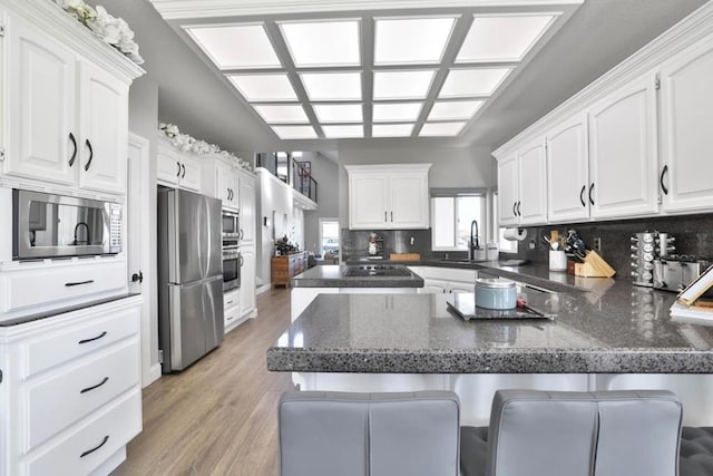 kitchen with appliances with stainless steel finishes, kitchen peninsula, a breakfast bar area, and white cabinets