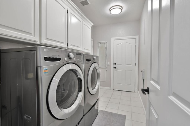 clothes washing area with cabinets, washing machine and dryer, and light tile patterned flooring