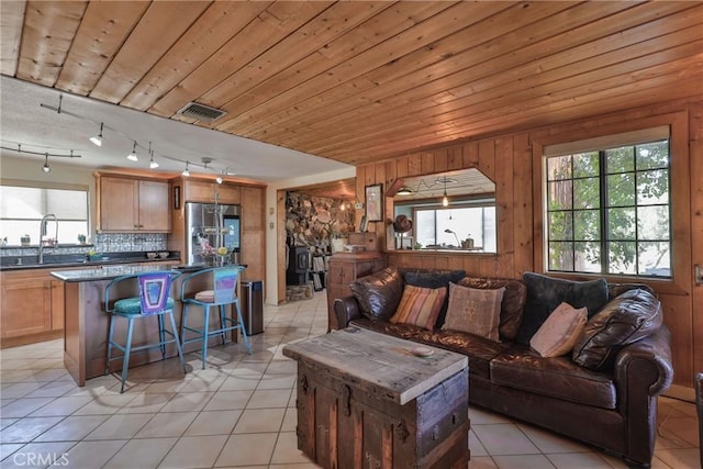 living room featuring light tile patterned flooring, sink, wooden walls, and wood ceiling