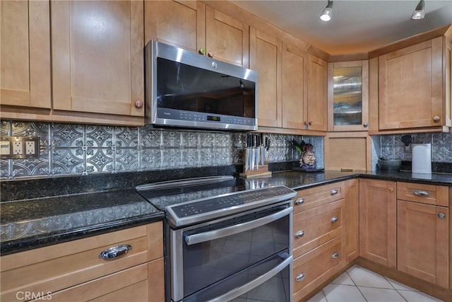 kitchen with tasteful backsplash, stainless steel appliances, light tile patterned floors, and dark stone countertops