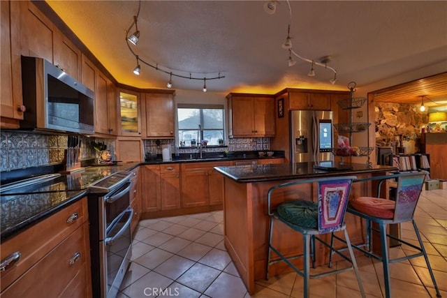 kitchen featuring a breakfast bar, sink, a center island, dark stone counters, and stainless steel appliances