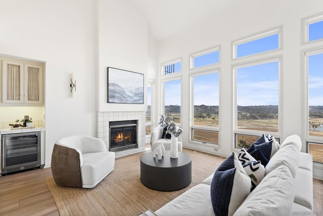 living room with wine cooler, a tiled fireplace, light hardwood / wood-style flooring, and a high ceiling