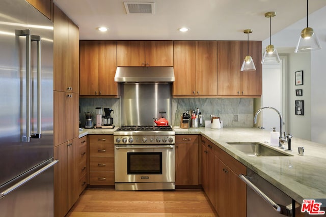 kitchen with sink, hanging light fixtures, high end appliances, light stone countertops, and light hardwood / wood-style flooring