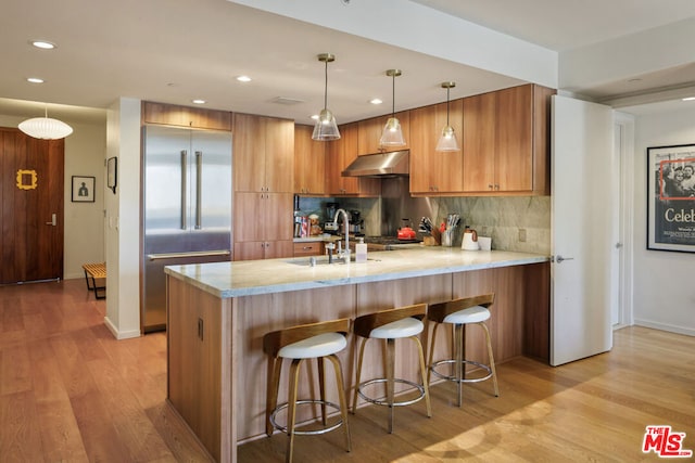 kitchen with hanging light fixtures, backsplash, a kitchen breakfast bar, stainless steel built in refrigerator, and kitchen peninsula