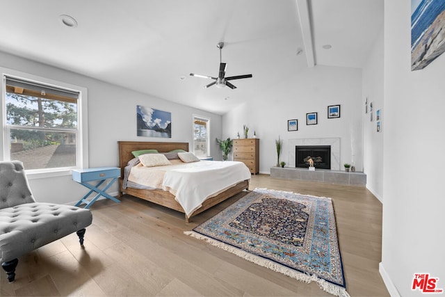 bedroom featuring beamed ceiling, high vaulted ceiling, a tile fireplace, and light wood-type flooring