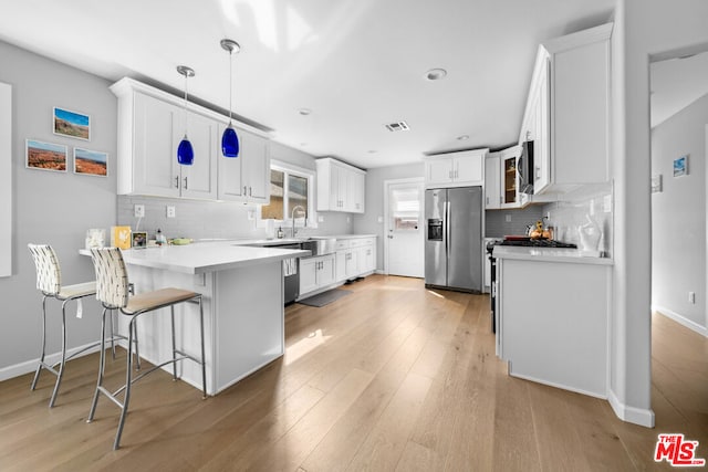 kitchen featuring pendant lighting, white cabinetry, stainless steel appliances, a kitchen bar, and kitchen peninsula