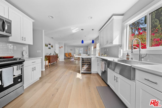 kitchen featuring sink, appliances with stainless steel finishes, hanging light fixtures, white cabinets, and beverage cooler