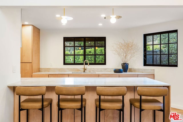 kitchen with a kitchen breakfast bar, kitchen peninsula, sink, and light wood-type flooring