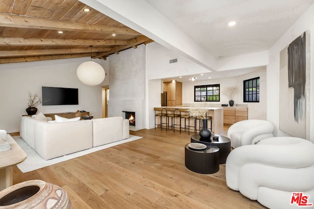 living room featuring lofted ceiling with beams, a large fireplace, wood ceiling, and light hardwood / wood-style floors