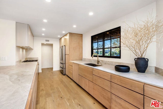 kitchen with high quality fridge, light brown cabinetry, sink, light stone countertops, and light wood-type flooring