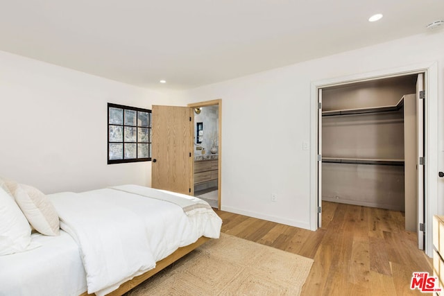 bedroom featuring a closet, a spacious closet, ensuite bathroom, and light hardwood / wood-style flooring