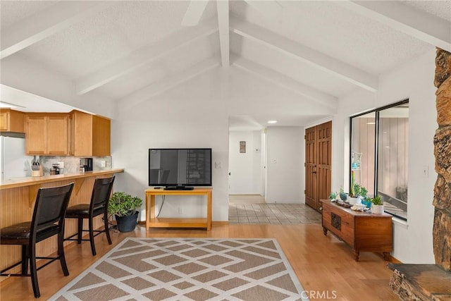 interior space with tasteful backsplash, vaulted ceiling with beams, a breakfast bar area, white refrigerator, and light hardwood / wood-style floors