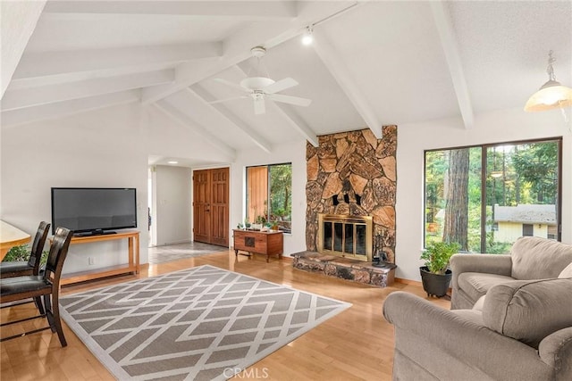 living room featuring lofted ceiling with beams, wood-type flooring, plenty of natural light, and a stone fireplace