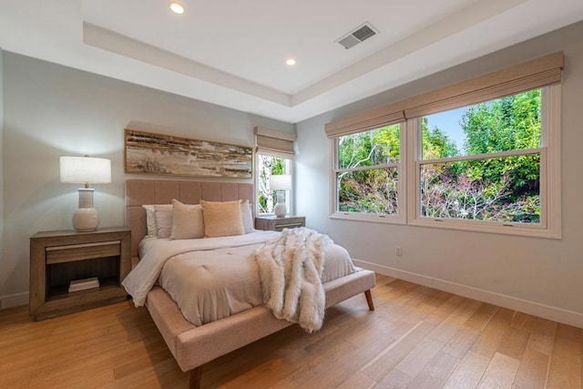 bedroom with light hardwood / wood-style flooring and a raised ceiling