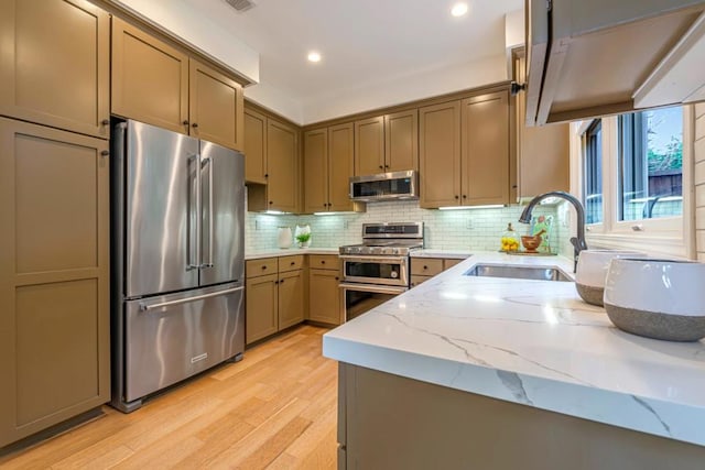 kitchen featuring sink, light hardwood / wood-style flooring, appliances with stainless steel finishes, tasteful backsplash, and light stone countertops