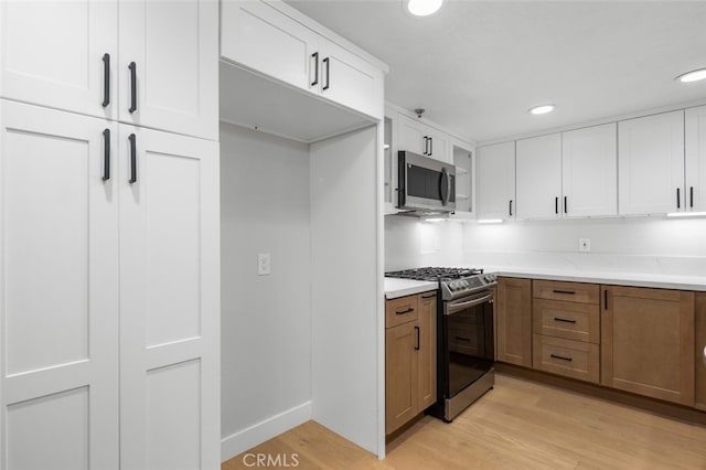 kitchen featuring white cabinetry, appliances with stainless steel finishes, light stone counters, and light wood-type flooring