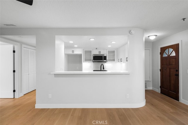 kitchen with light hardwood / wood-style floors, kitchen peninsula, sink, and white cabinets