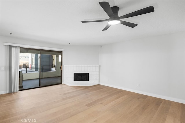 unfurnished living room featuring a brick fireplace, ceiling fan, and light wood-type flooring