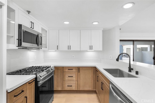 kitchen with sink, white cabinetry, light stone counters, light wood-type flooring, and stainless steel appliances