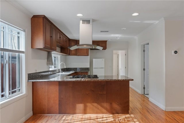 kitchen with island range hood, sink, white fridge, stainless steel gas cooktop, and kitchen peninsula