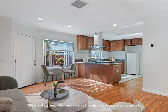 kitchen featuring white refrigerator, ornamental molding, island exhaust hood, dark stone counters, and light hardwood / wood-style floors