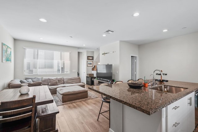 kitchen featuring sink, a center island with sink, light wood-type flooring, a kitchen breakfast bar, and white cabinets