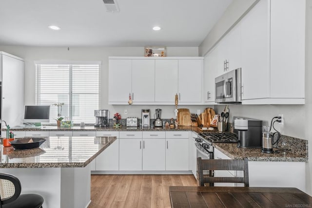 kitchen featuring light hardwood / wood-style floors, dark stone counters, white cabinets, and appliances with stainless steel finishes