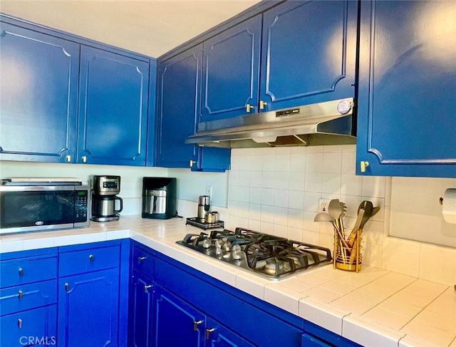 kitchen with blue cabinets, stainless steel appliances, tile countertops, and decorative backsplash