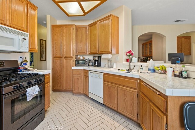 kitchen with white appliances, tile countertops, kitchen peninsula, and sink