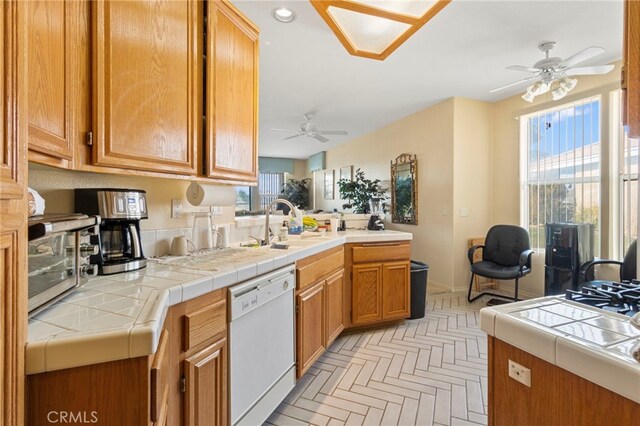 kitchen with white dishwasher, light parquet floors, tile counters, and a healthy amount of sunlight