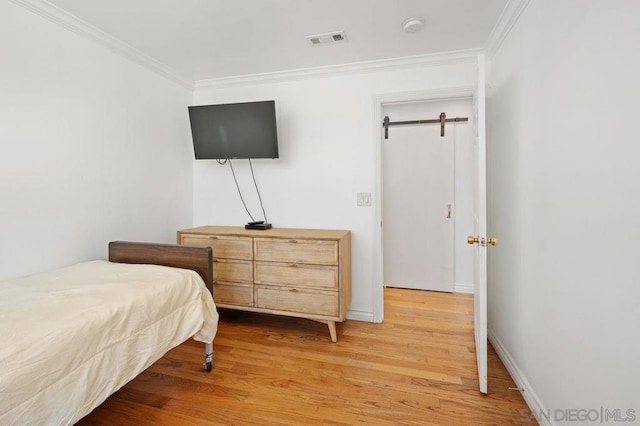 bedroom with crown molding, a barn door, and light hardwood / wood-style floors