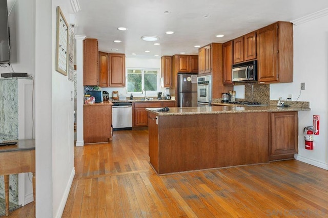 kitchen with sink, kitchen peninsula, stone counters, stainless steel appliances, and light hardwood / wood-style floors