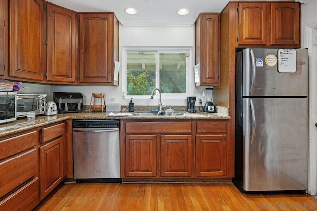 kitchen featuring appliances with stainless steel finishes, stone countertops, sink, ornamental molding, and light hardwood / wood-style floors